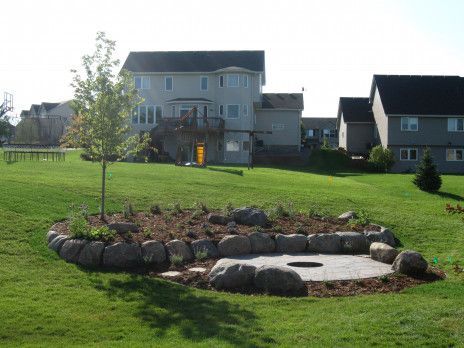 Suburban backyard with a stone fire pit surrounded by grass and a house in the background