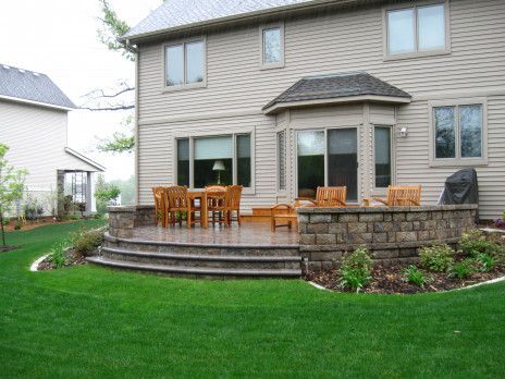 Backyard patio with wooden dining set, stone steps, and lush green lawn behind a house
