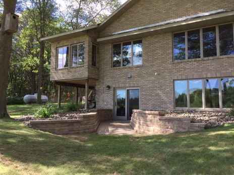 Two-story brick house with large windows, a raised back patio, and a wooded yard