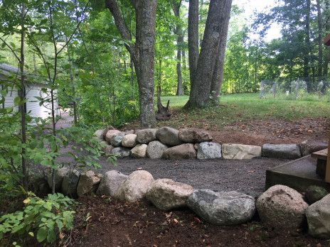 Rock-bordered gravel path in a wooded yard with trees and green grass