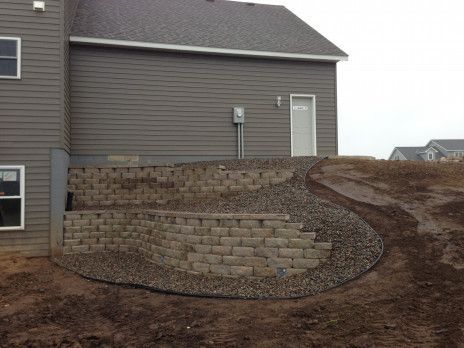 Landscaped retaining wall beside a gray house on a dirt slope