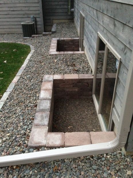 Backyard basement window wells lined with brick blocks and gravel beside a house