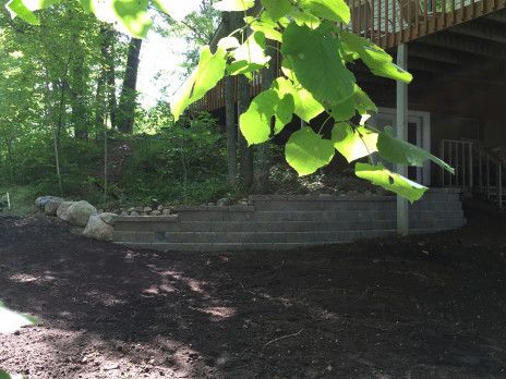 Shaded backyard with a deck, stone retaining wall, and bright green leaves overhead