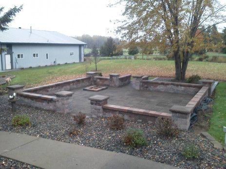Raised wooden garden beds in a backyard beside a white building and trees, with gravel and grass surrounding them.