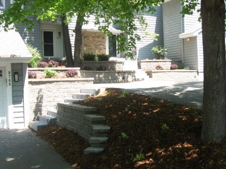 White house front porch with stone steps, retaining wall, and shaded yard under trees