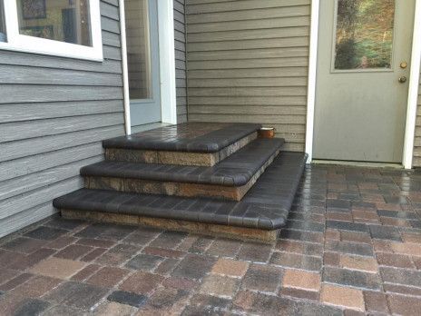 Front porch with brick pavers, gray siding, and stacked outdoor cushions by the door