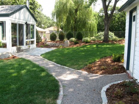 Curved stone path through a green garden beside a white house and glass sunroom
