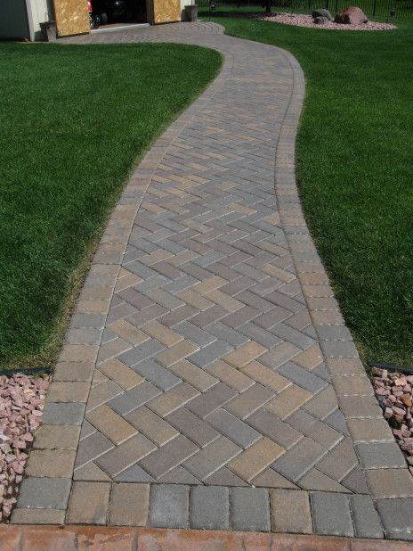 Curved brick walkway bordered by green grass and edging stones in a landscaped yard