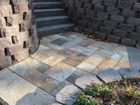 Stone steps and curved brick retaining walls beside a tiled patio with a small patch of plants