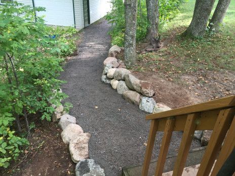 Garden path edged with rocks beside trees and a wooden railing leading to a white building