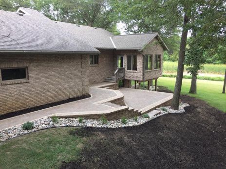 Brick house with curved stone walkway, small porch, and dark mulch landscaping in a wooded yard