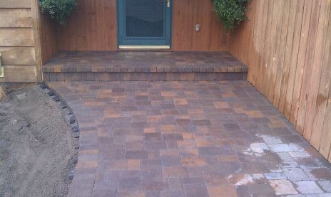 Brick-paved patio leading to a doorway, bordered by wood fences and a small dirt patch