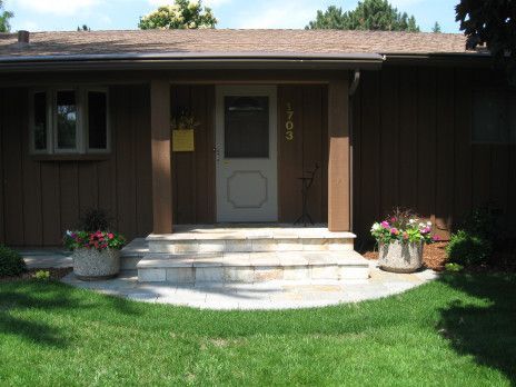 Front porch of a house with steps, potted flowers, and a green lawn.