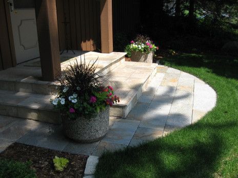 Front porch with stone steps, potted flowers, and sunlight on a grassy yard