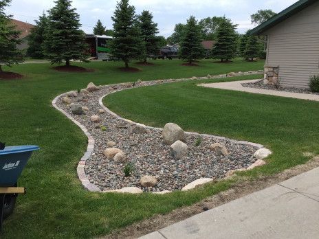 Curved rock garden bed with gravel and boulders beside a sidewalk and lawn, near a house.