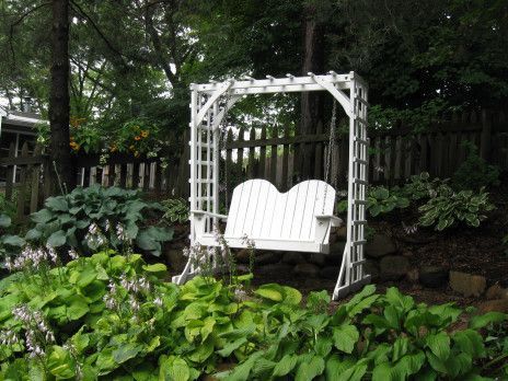 White garden swing under a white arbor in a lush, leafy backyard garden.