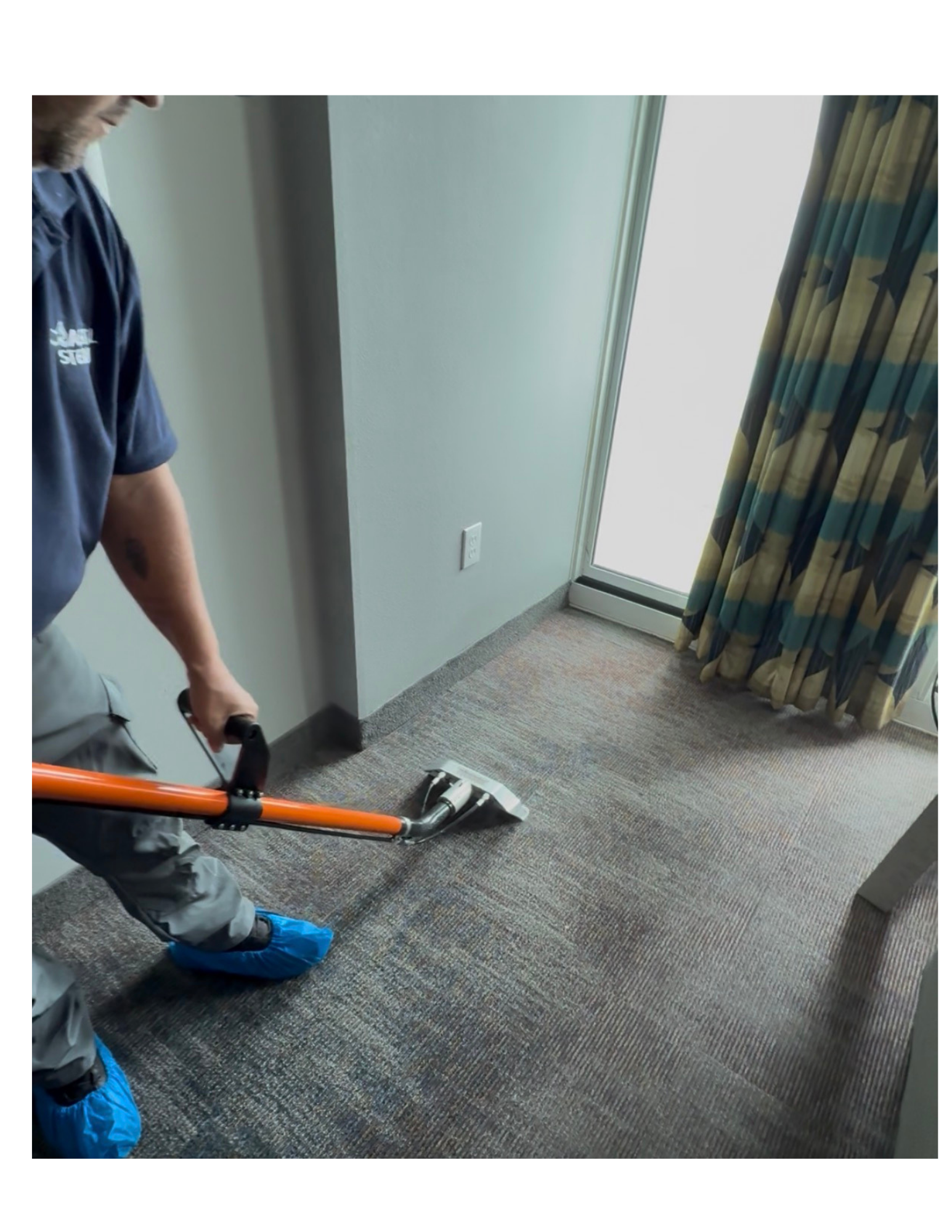 A person wearing a black glove uses a yellow power tool to clean a dark gray fabric sofa.