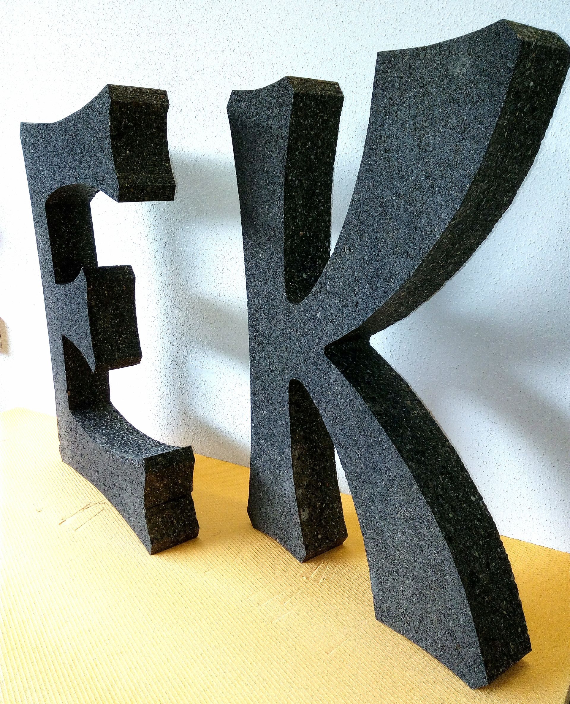 Ein großer schwarzer Buchstabe K liegt auf einem Tisch