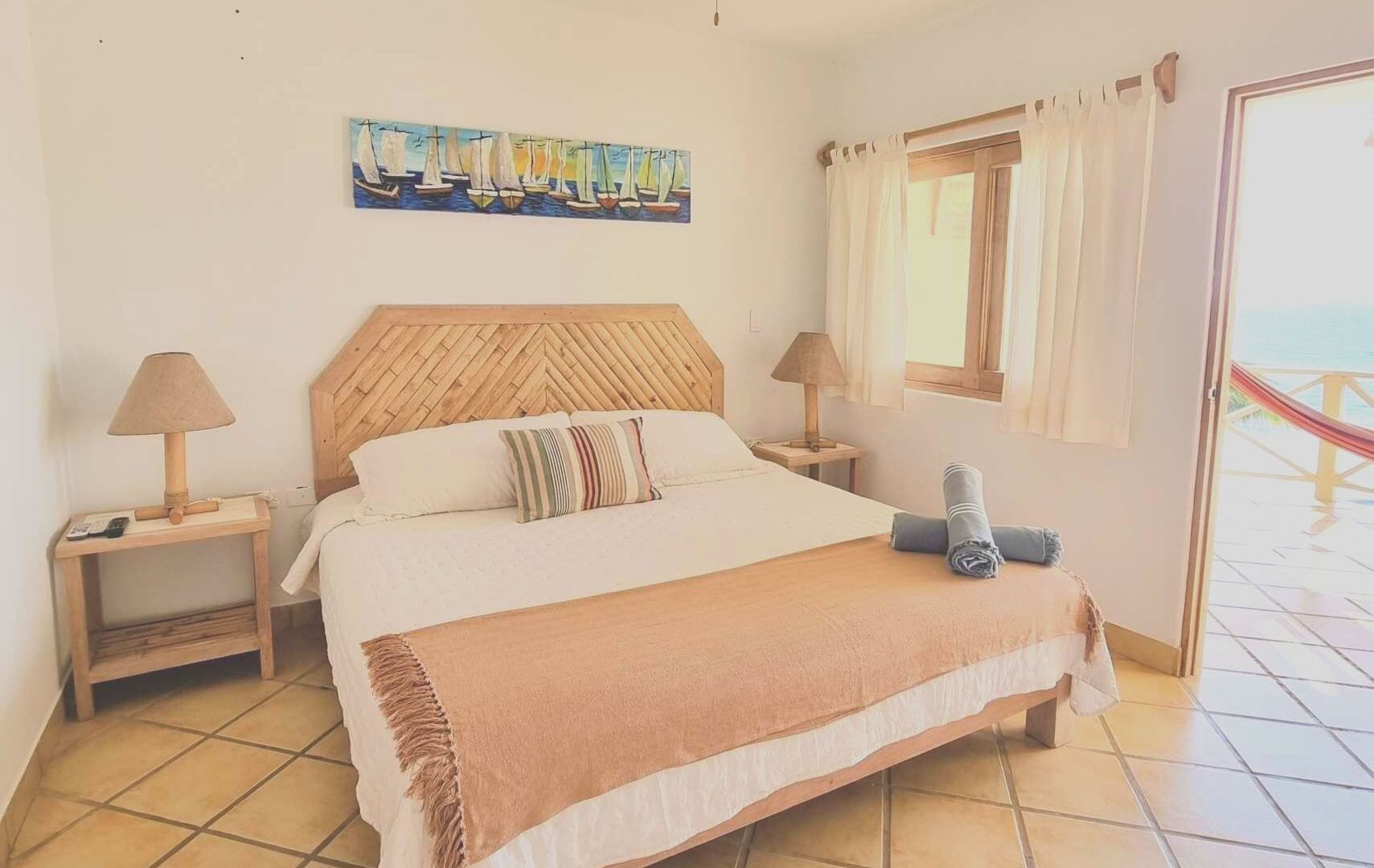 Bedroom with a bed, lamps, window, and door to a deck with a hammock, light colors.
