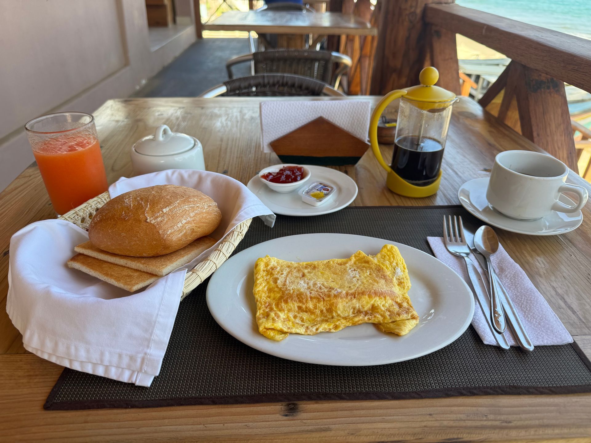 Breakfast spread on a wooden table: omelet, bread, toast, juice, coffee, jam, and butter.
