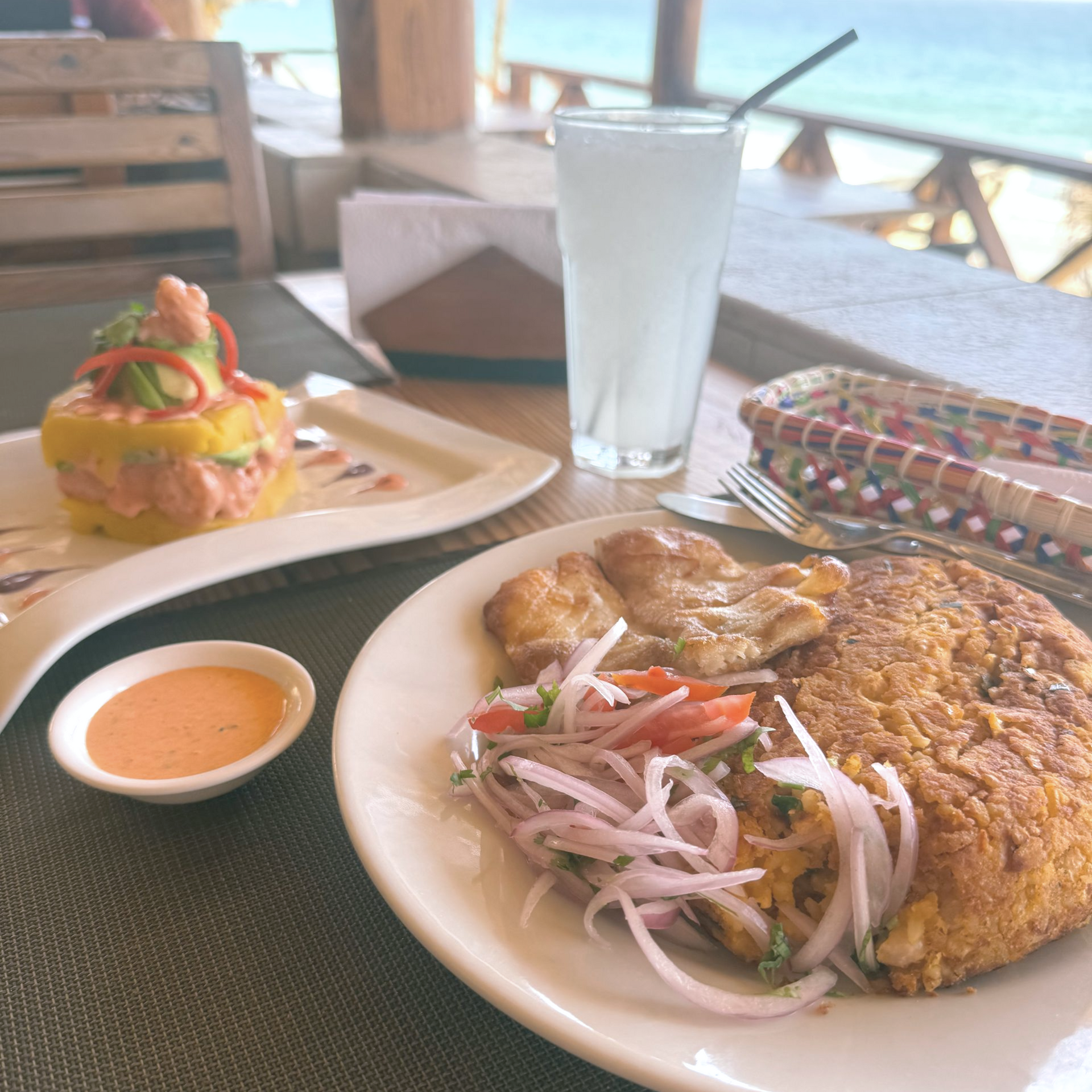 Table setting: fried fish, salad, shrimp tower, drink, seaside restaurant view.