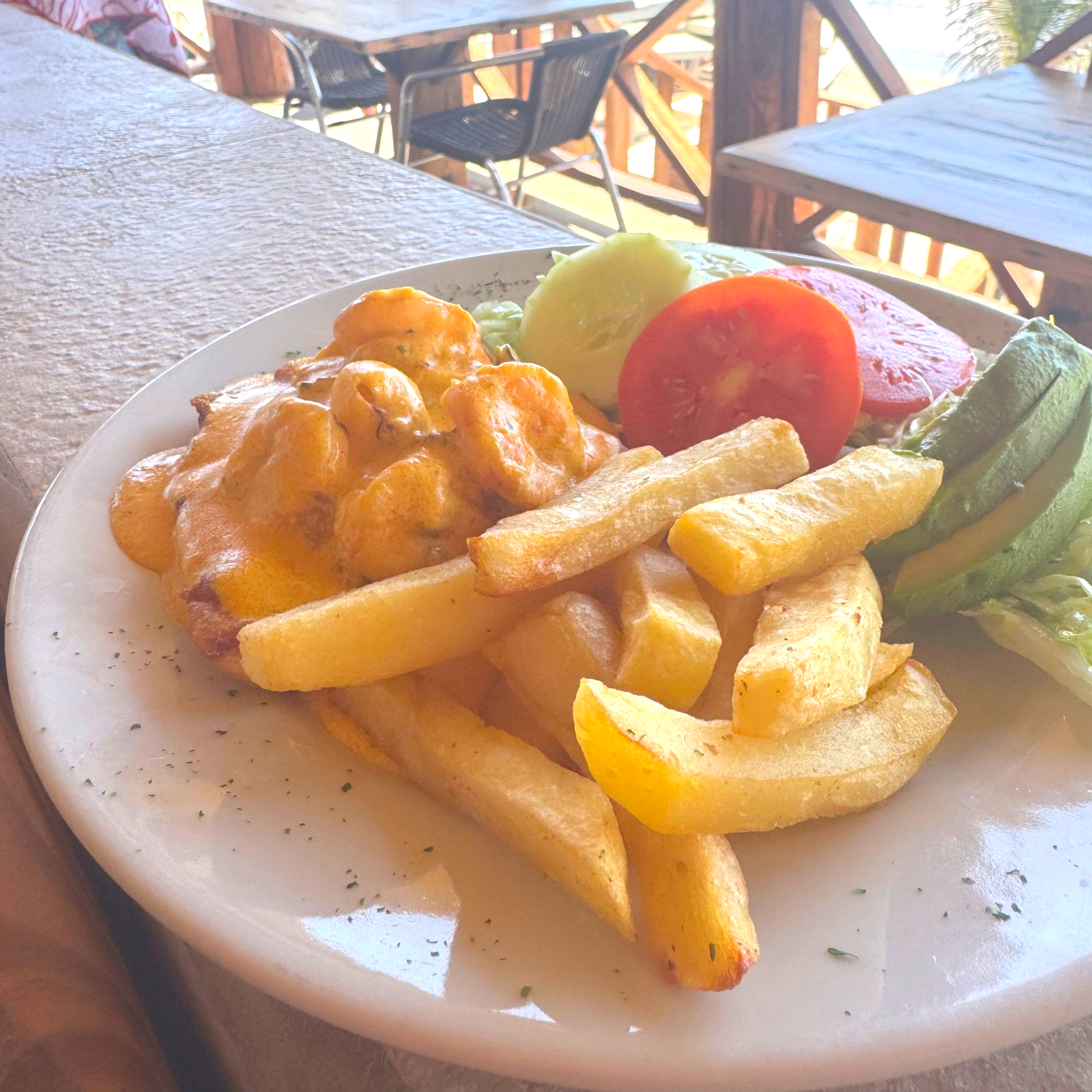 Plate of shrimp, fries, avocado, tomato, and cucumber; outdoor table setting.