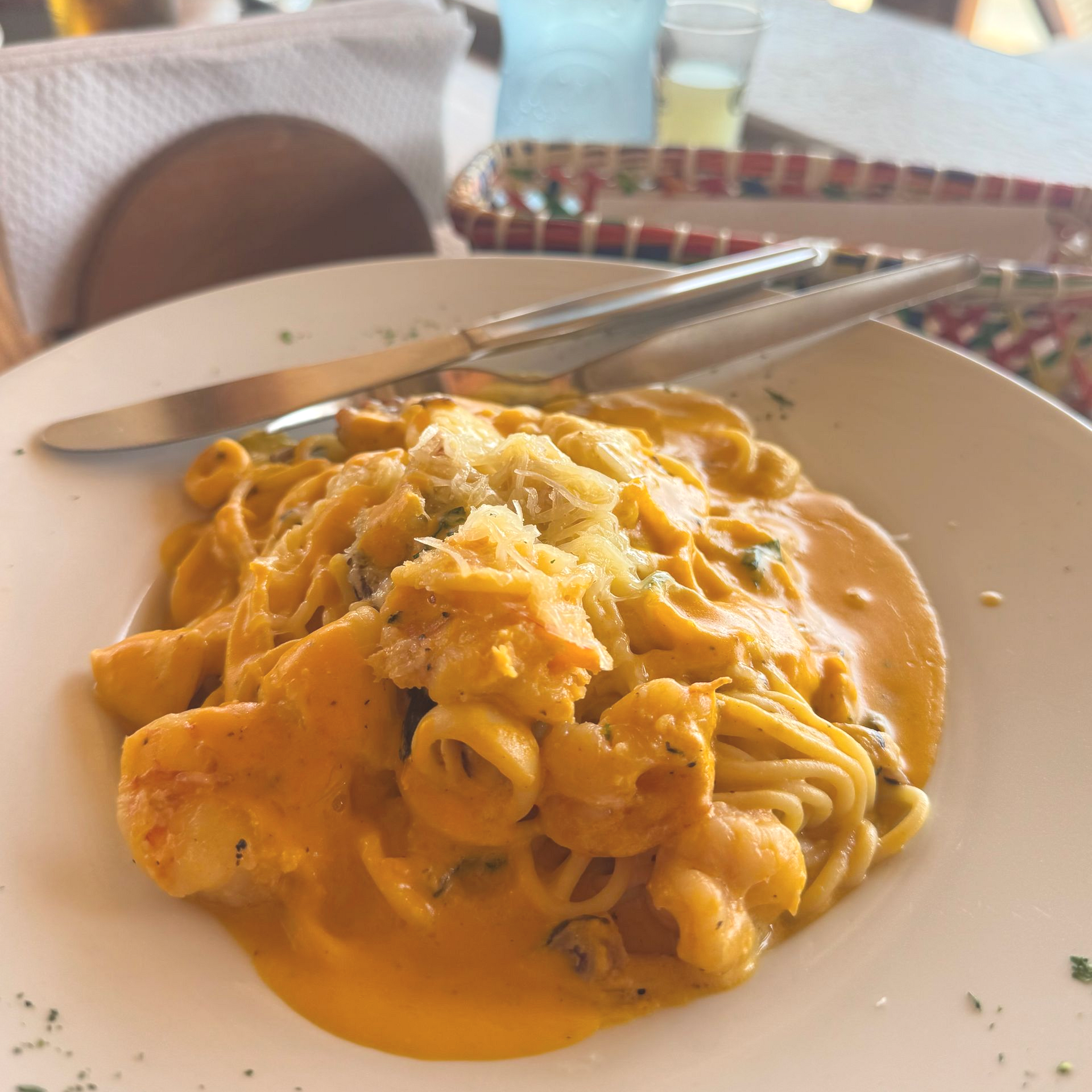 Pasta dish with orange sauce and grated cheese on a white plate with silverware, at a restaurant.
