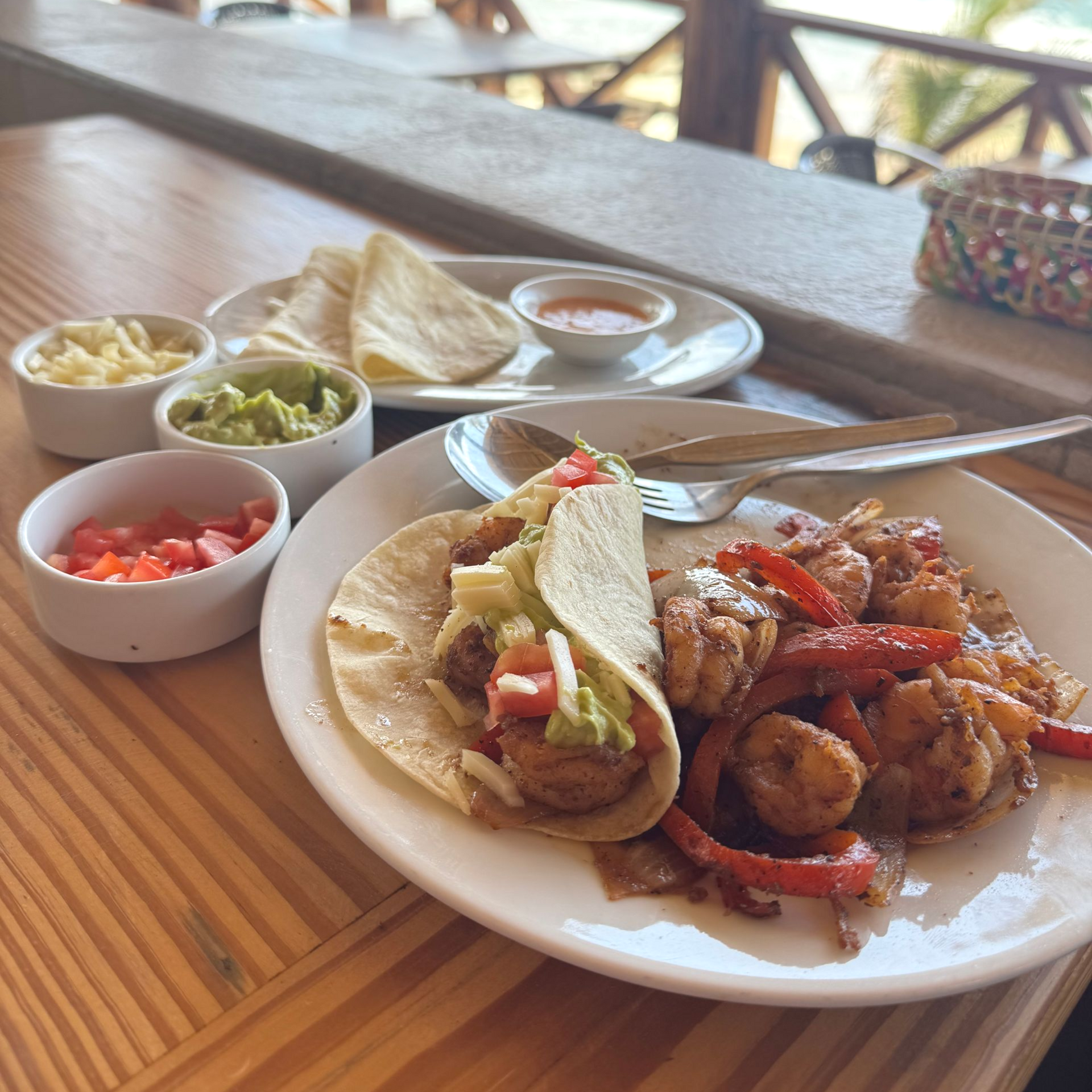 Plate of shrimp tacos, fajitas, and sides on a table at a restaurant.