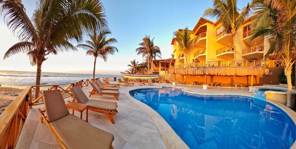 Tropical resort with pool, beach, palm trees, and a building with balconies.