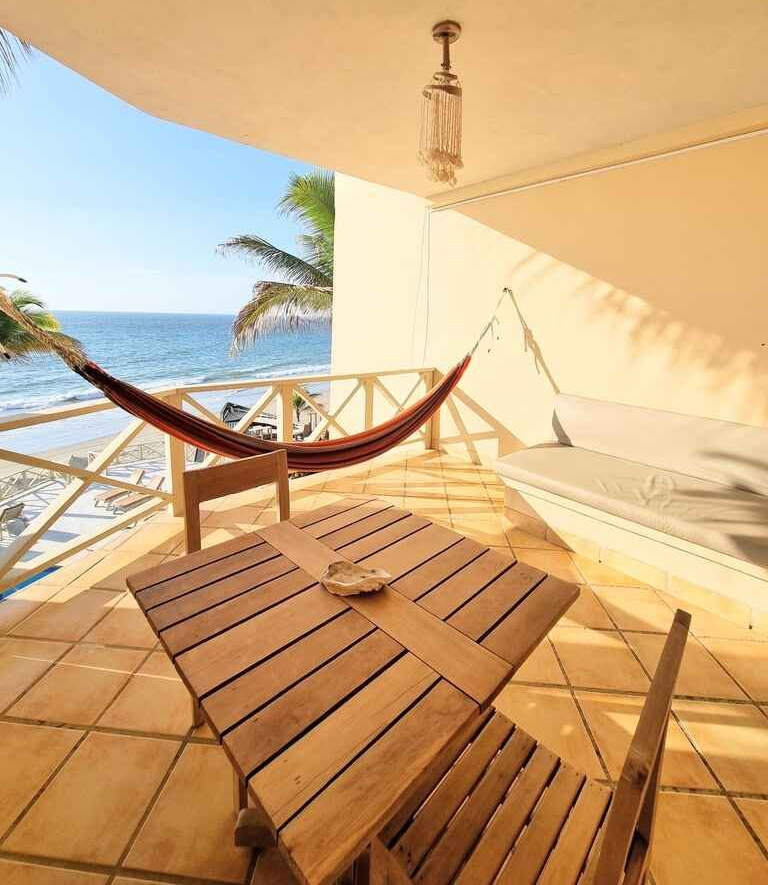 A balcony with a hammock and a table overlooking the ocean.