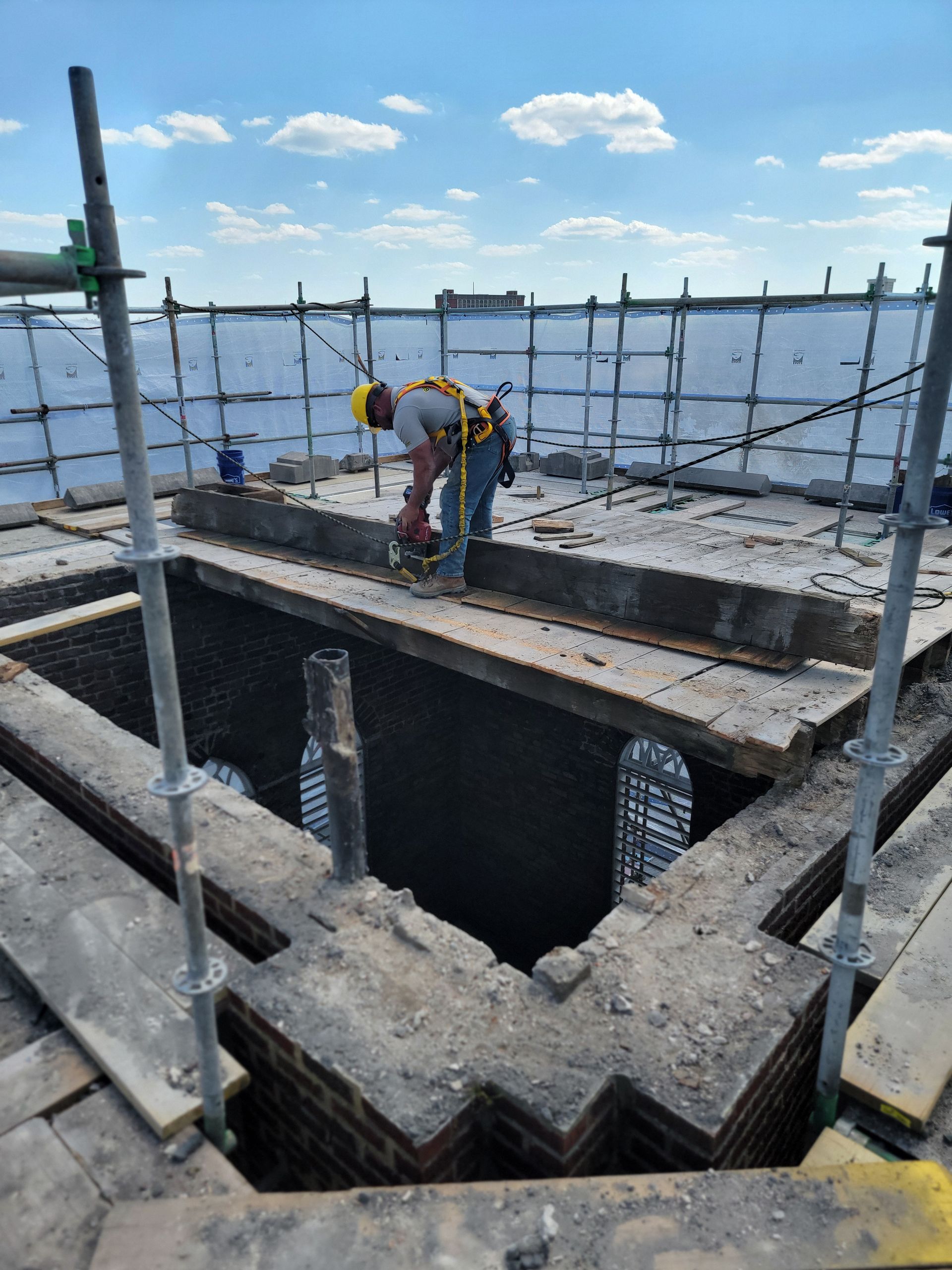 Worker in a hard hat bending over a concrete rooftop construction site with safety scaffolding.