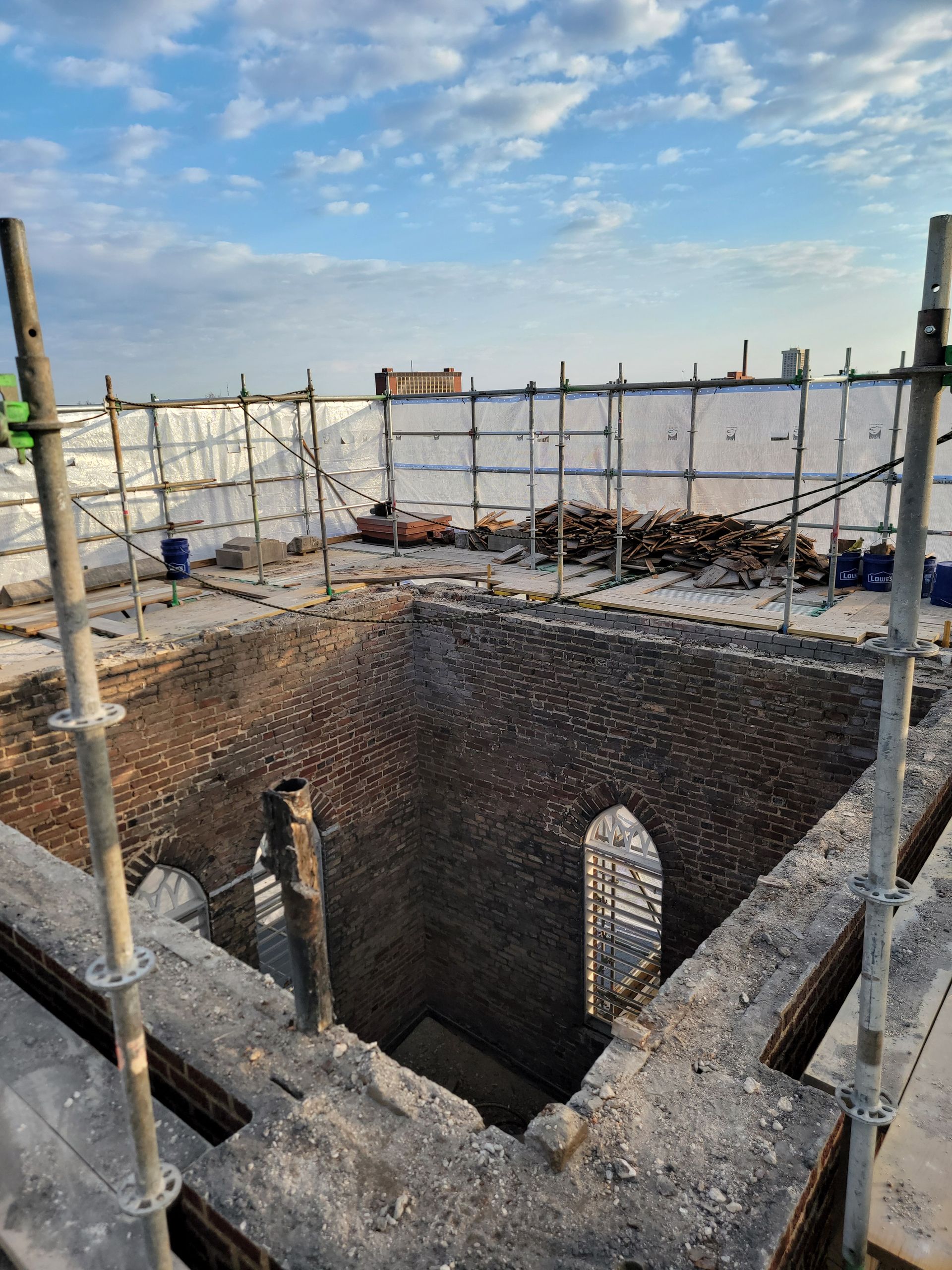 Stone-lined excavation pit at a construction site, surrounded by scaffolding and safety netting under a blue sky
