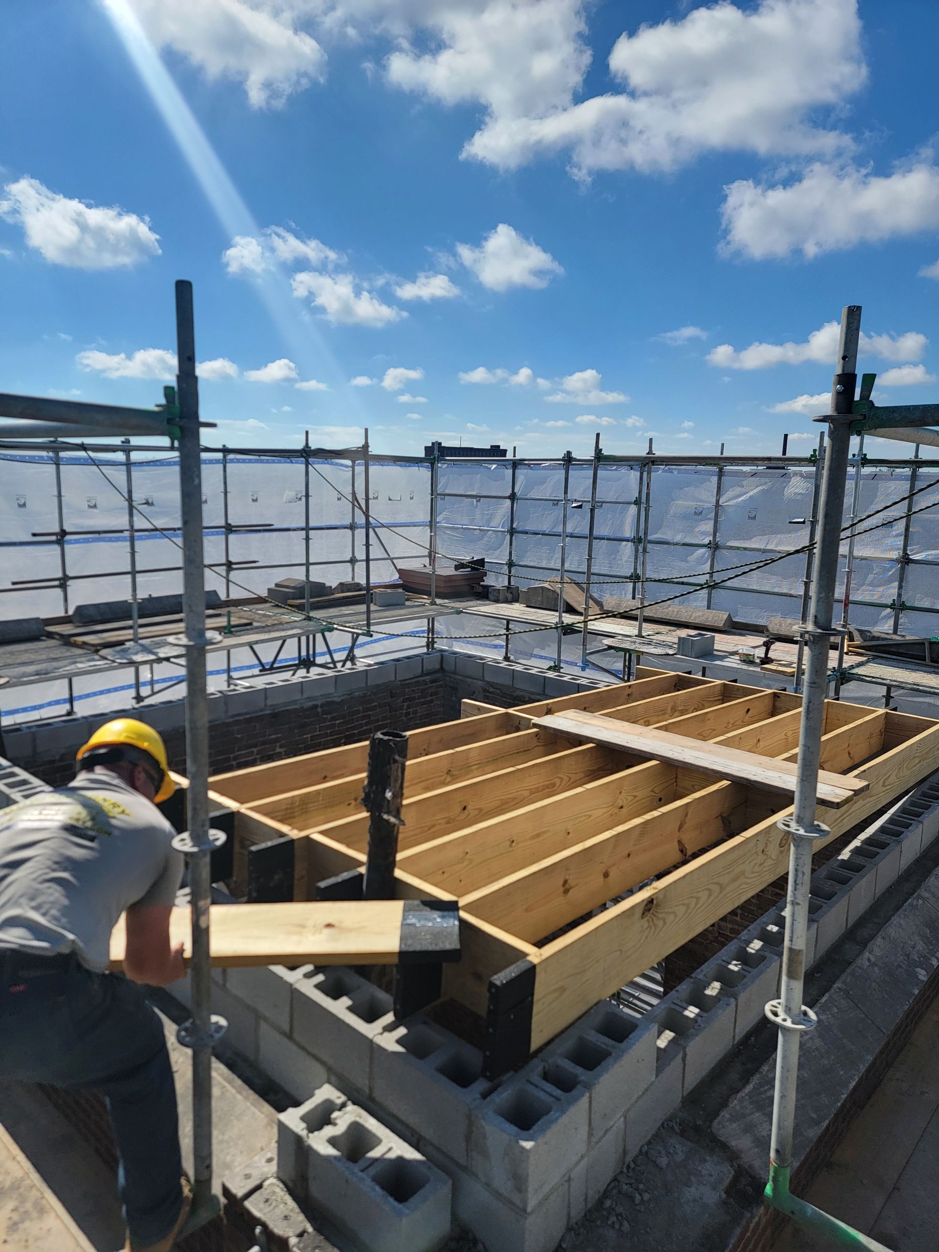 Worker pouring concrete into rooftop formwork under a blue sky