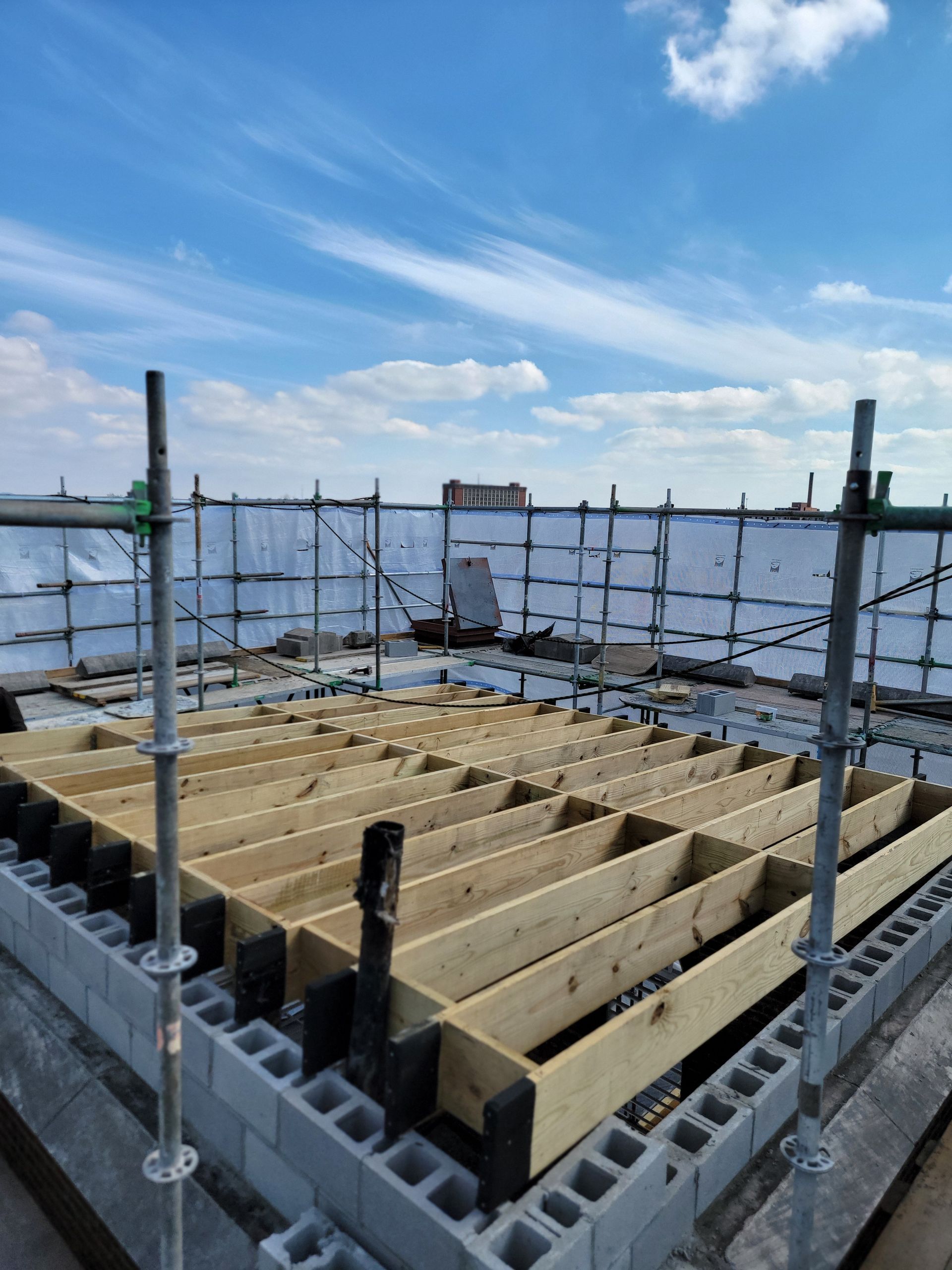 Scaffolding around a rooftop construction area with wooden framing under a blue sky