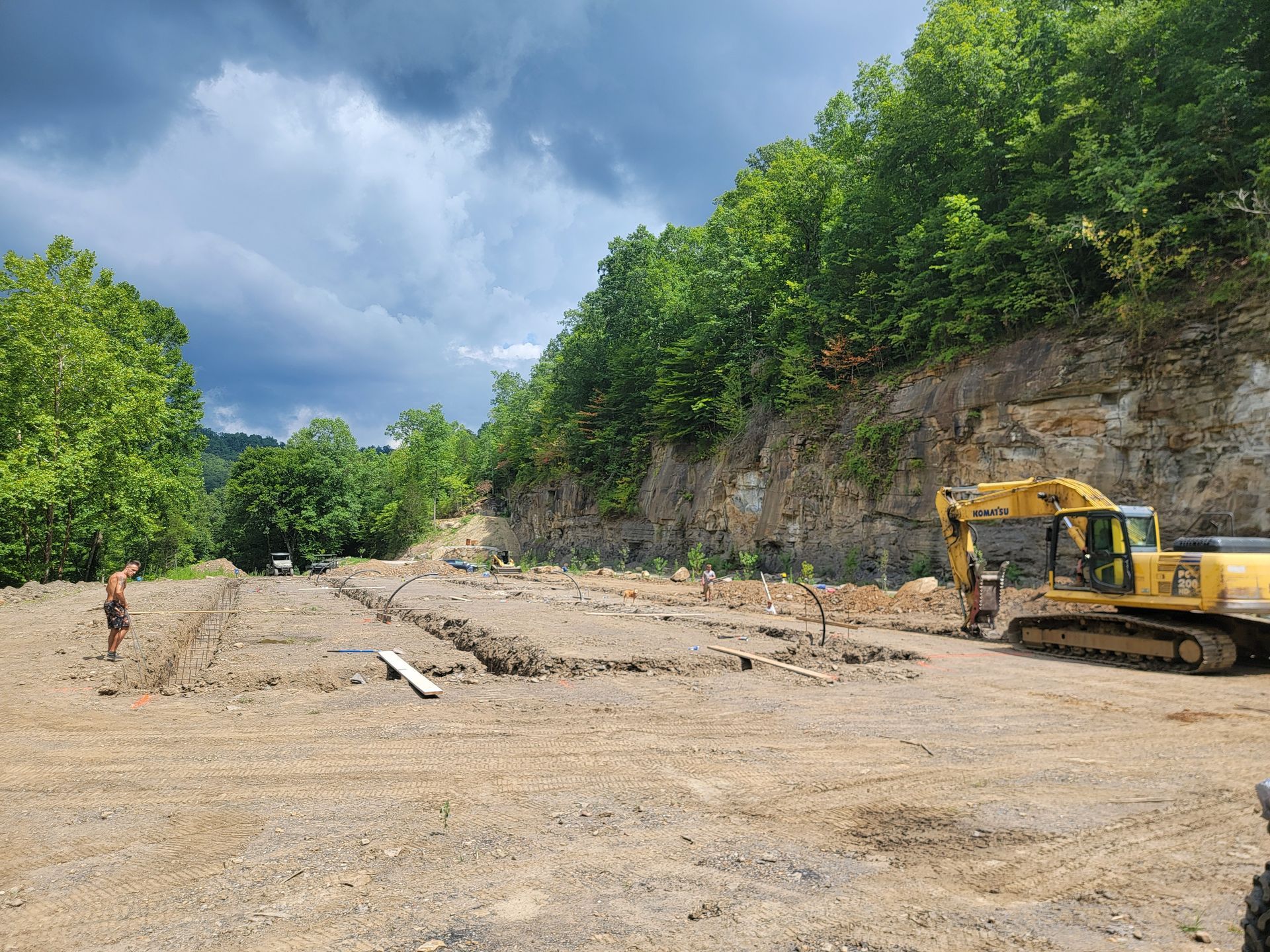 Construction site with excavator beside a rocky hillside under a cloudy sky