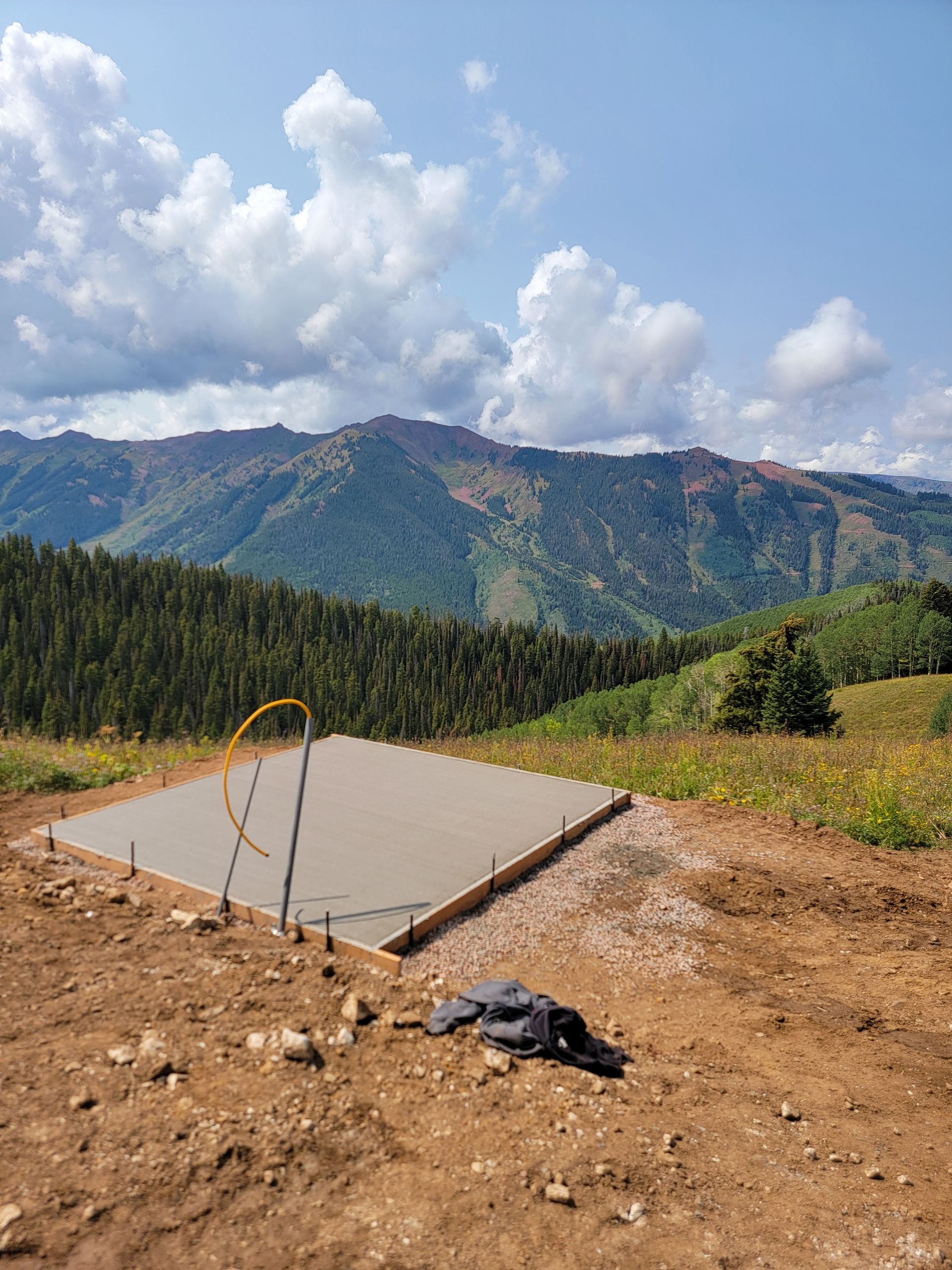 Concrete slab on a dirt hillside with mountains, forest, and cloudy blue sky in the background