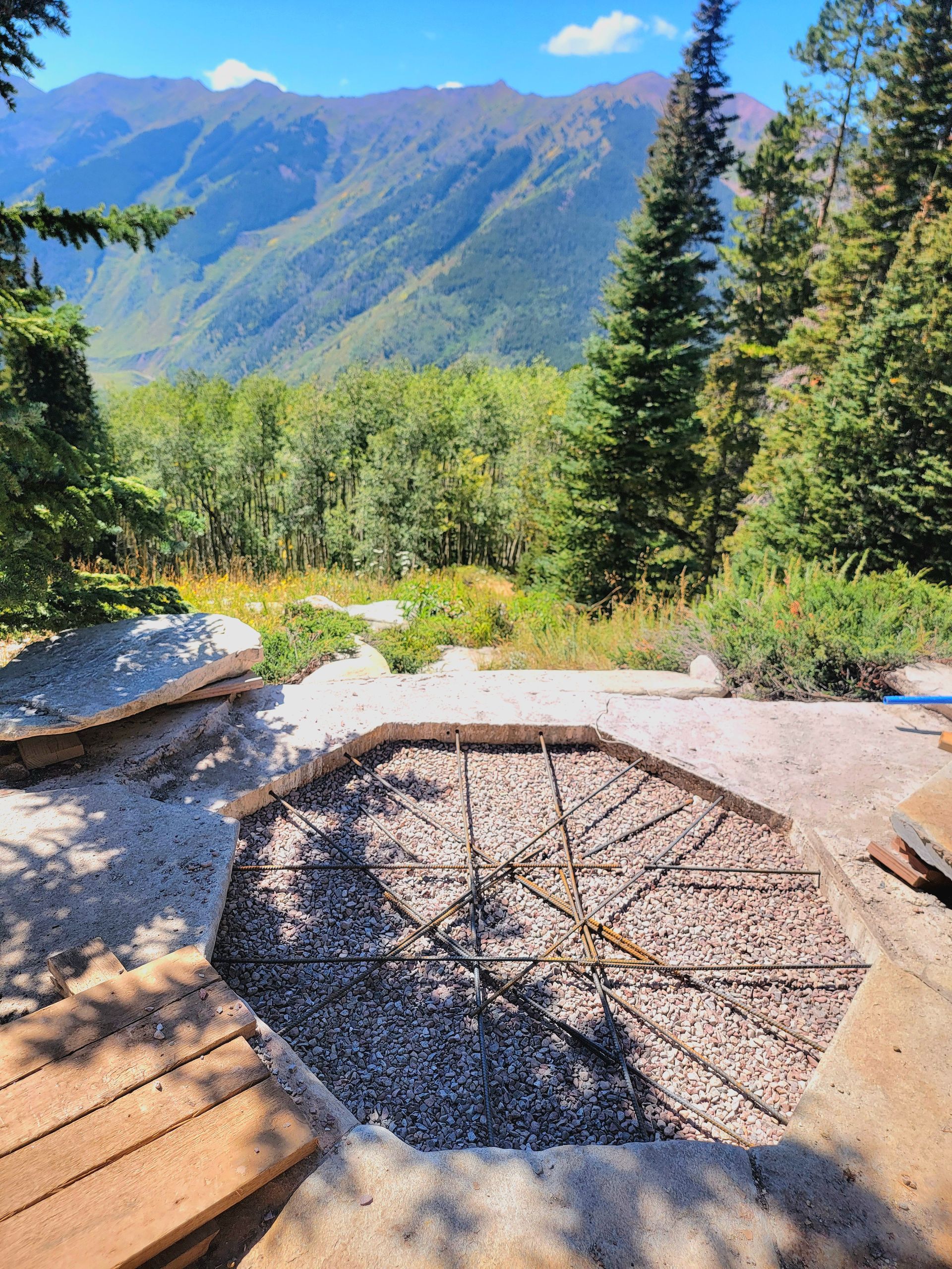 Stone fire pit on a mountain overlook with evergreen trees and distant blue peaks.