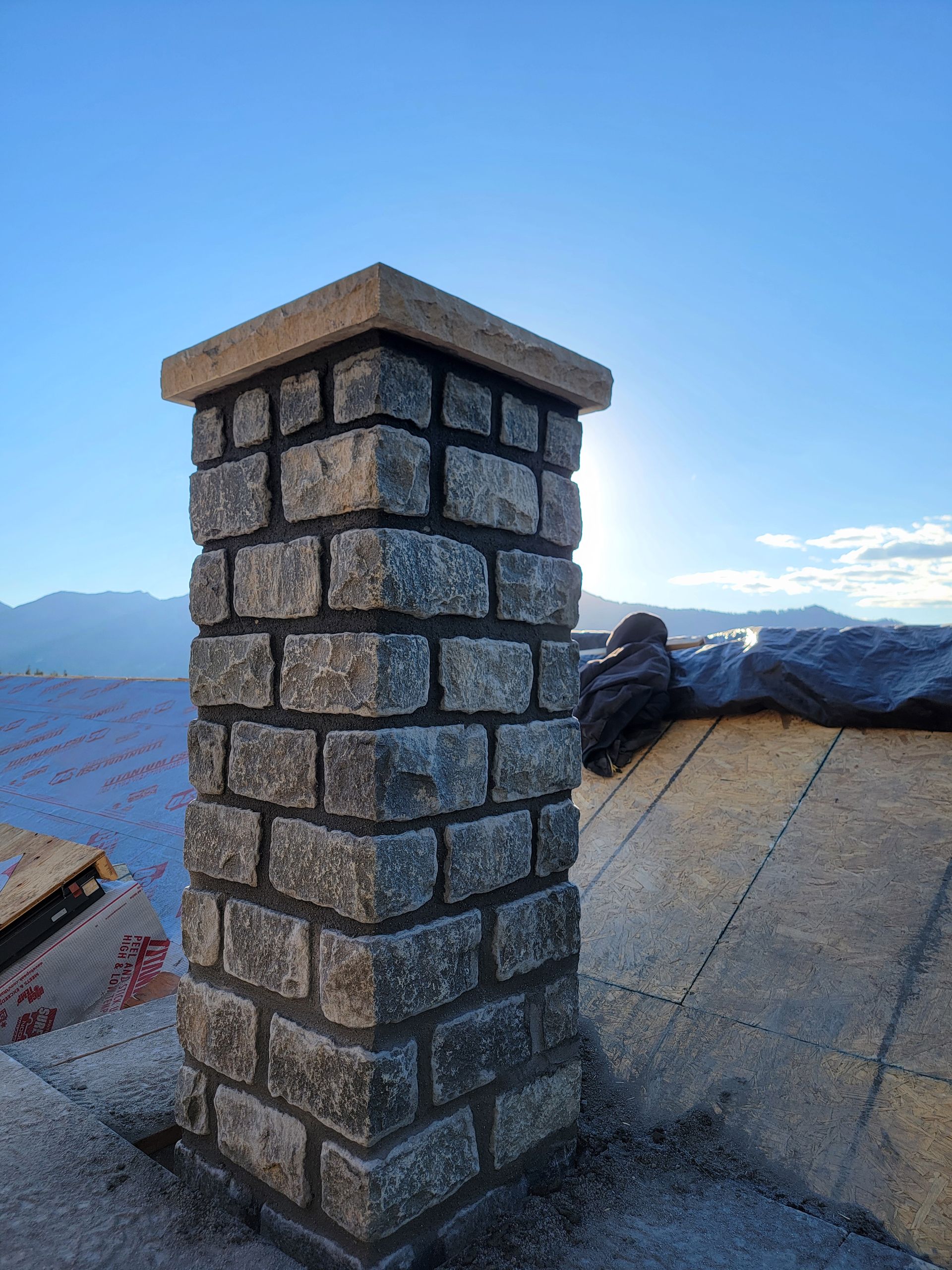 Stone chimney on a rooftop with mountains and blue sky in the background