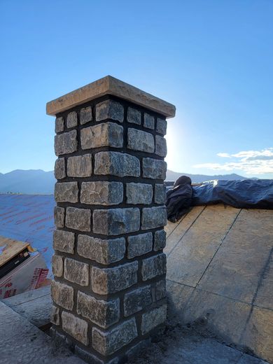 Stone chimney on a rooftop with mountains and blue sky in the background
