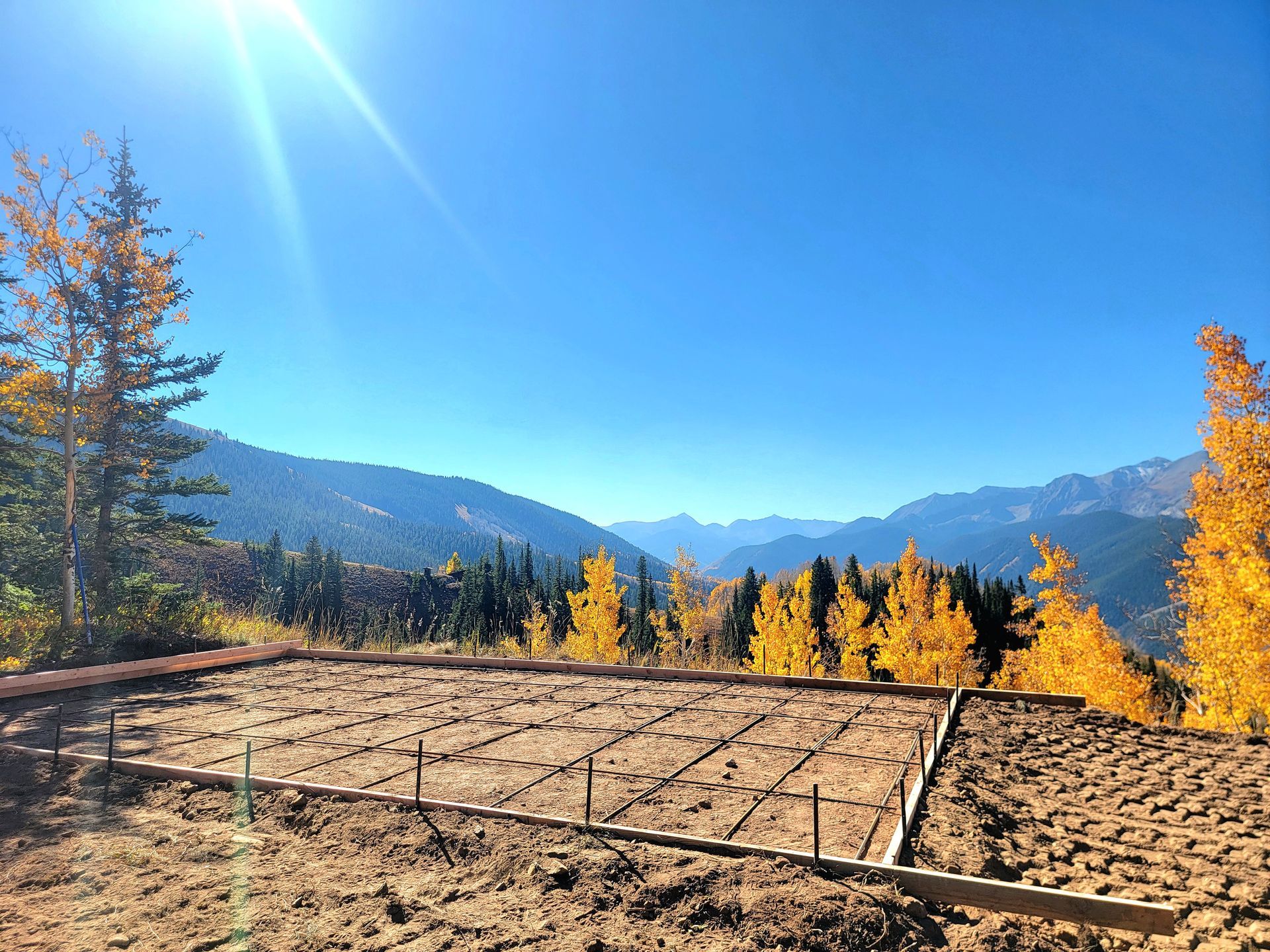 Autumn mountain landscape with a dry field, yellow trees, and blue sky