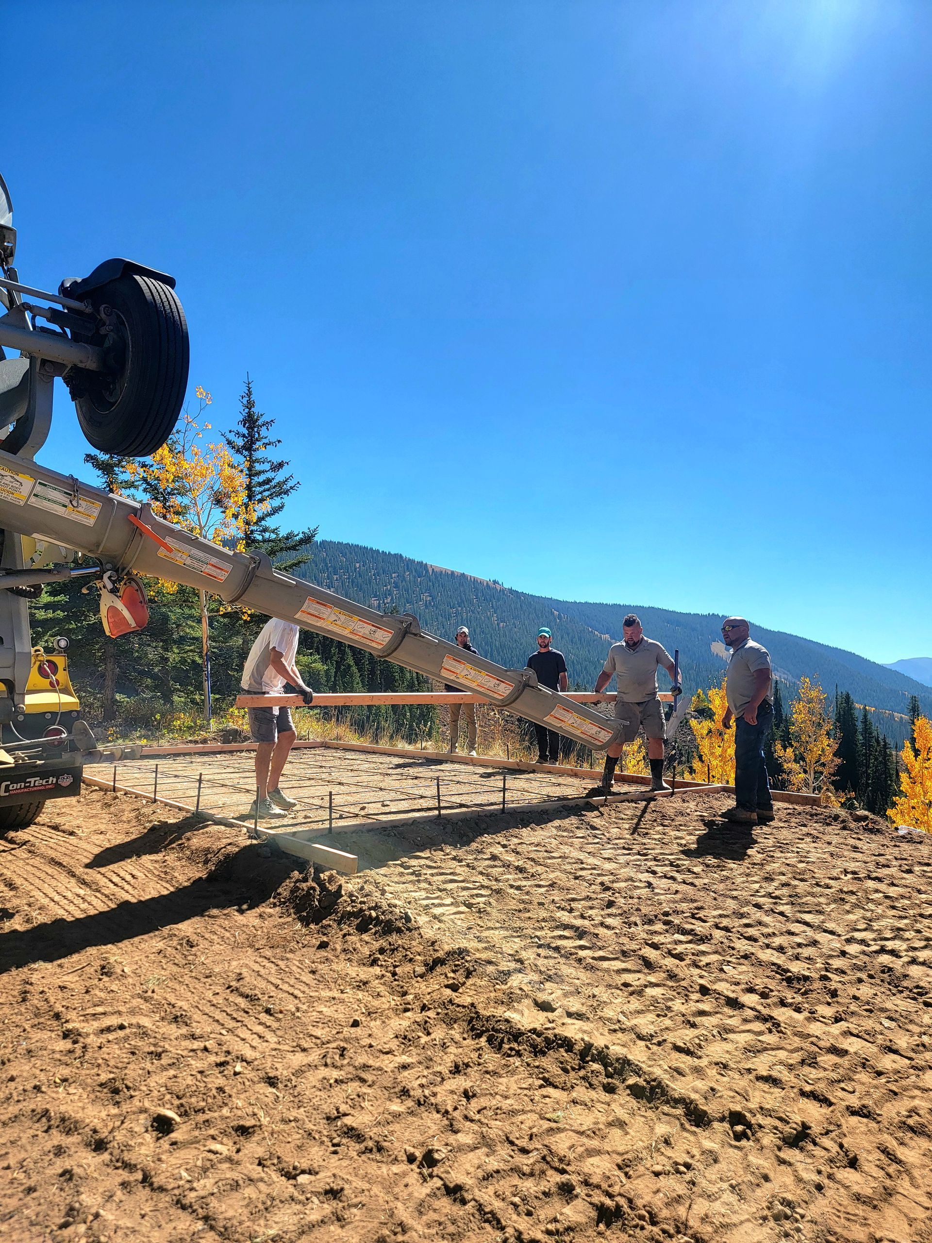 People standing by an off-road vehicle on a rocky mountain trail under a bright blue sky.