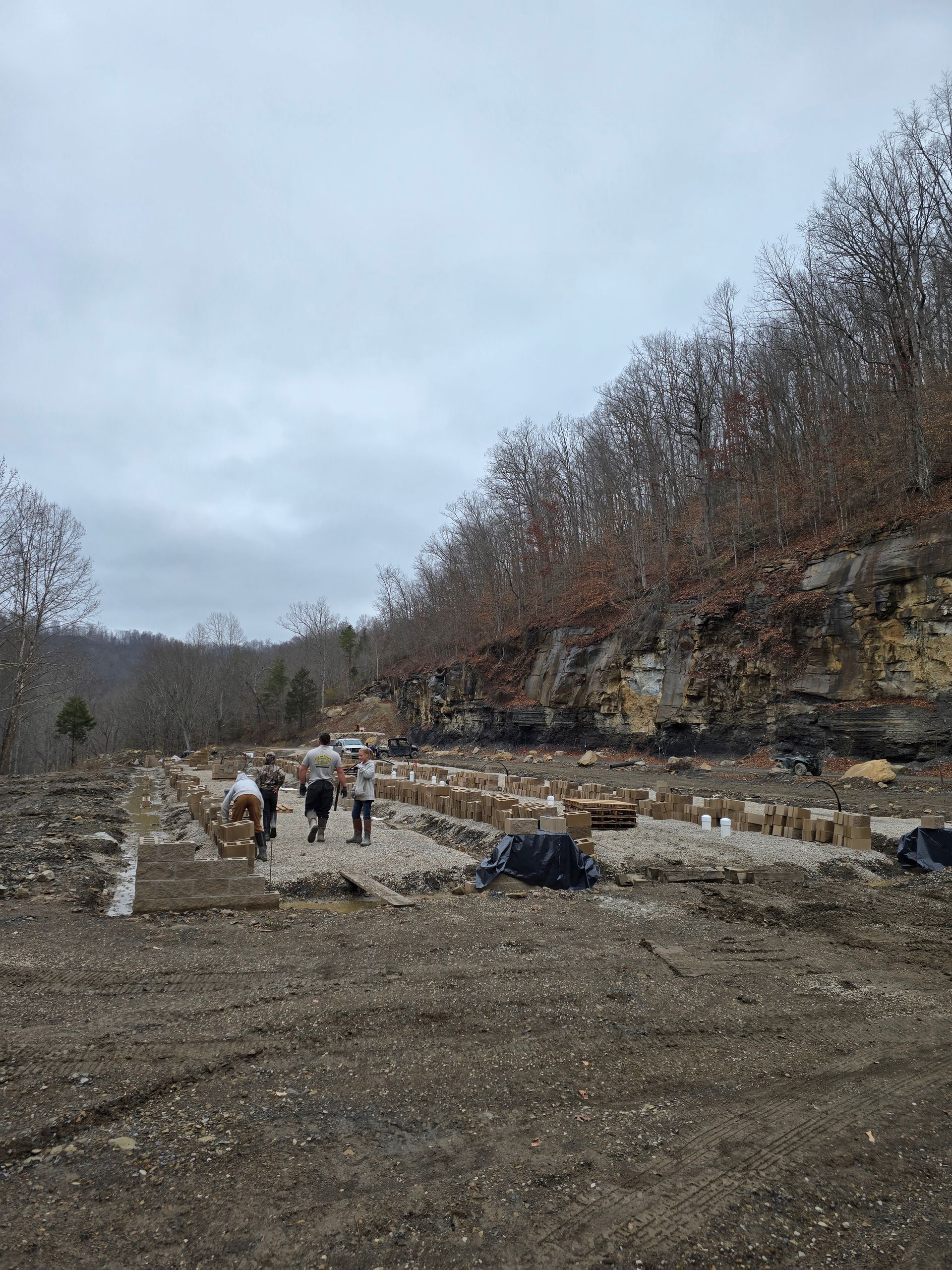 Rocky quarry with a few people walking near stone walls under a cloudy sky