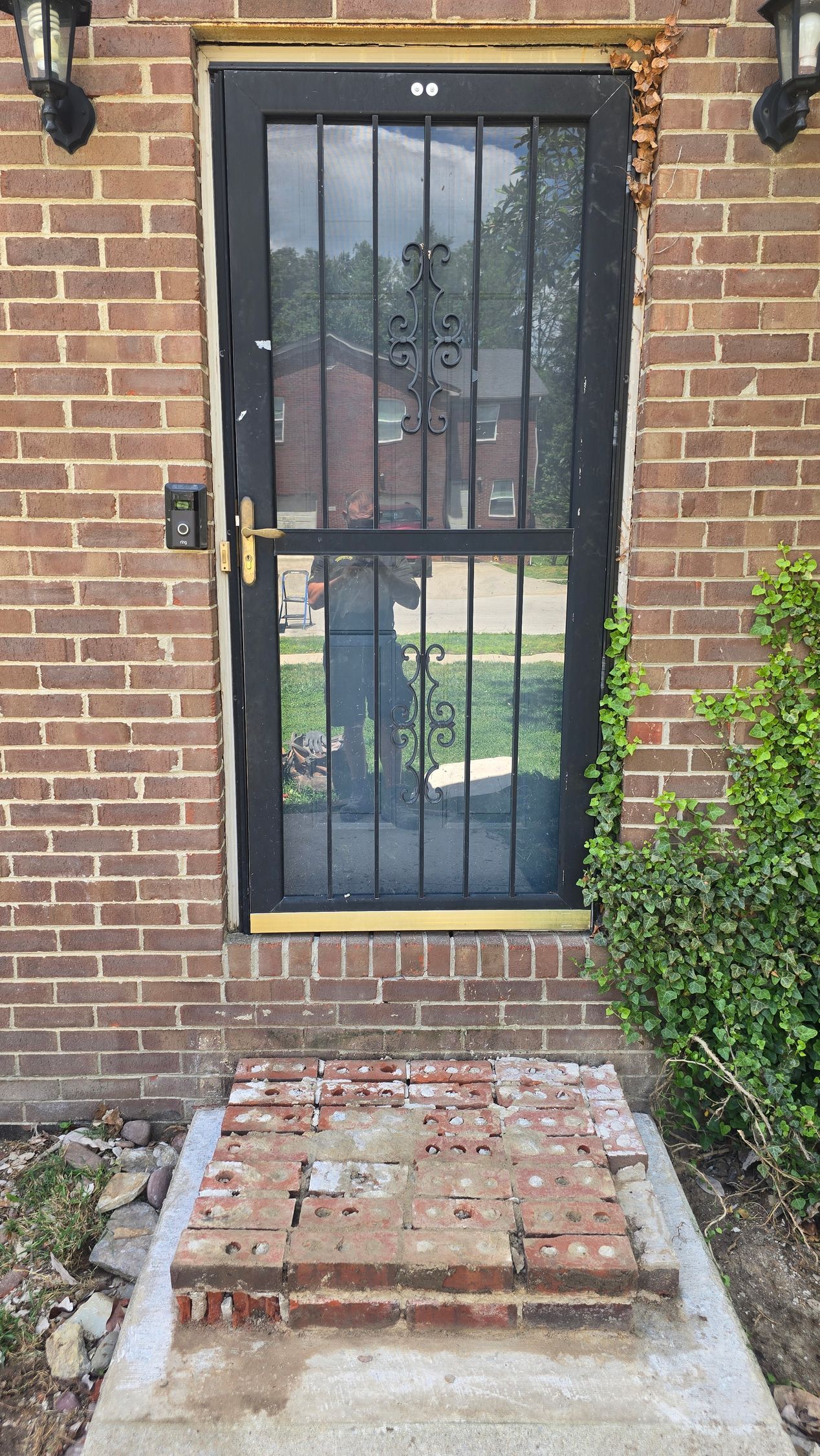 Brick wall with a black metal security door and a damaged brick stoop below.