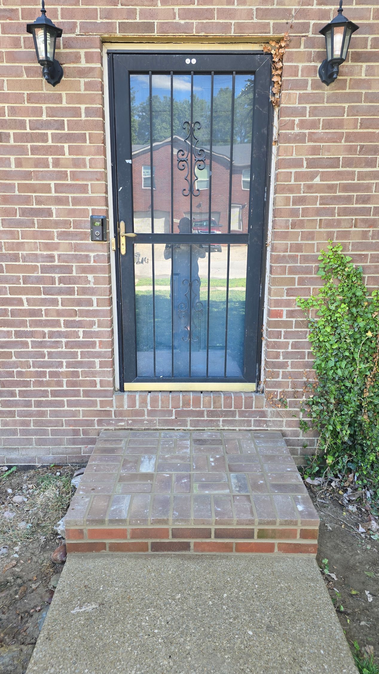 Brick house entry with a barred front door, two black lanterns, and a small brick step.