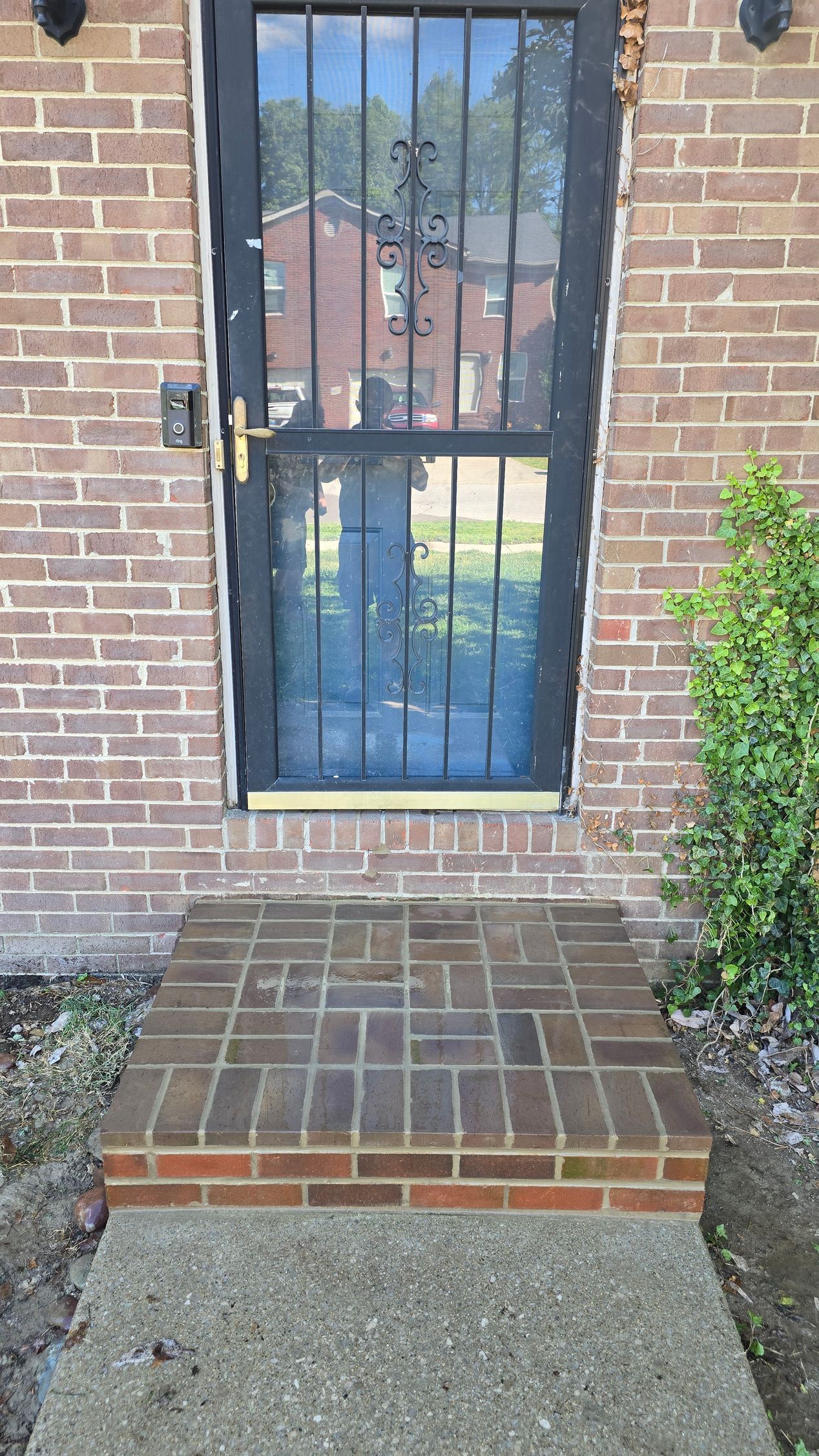 Brick front door with a black security screen and a small tiled step leading up to it