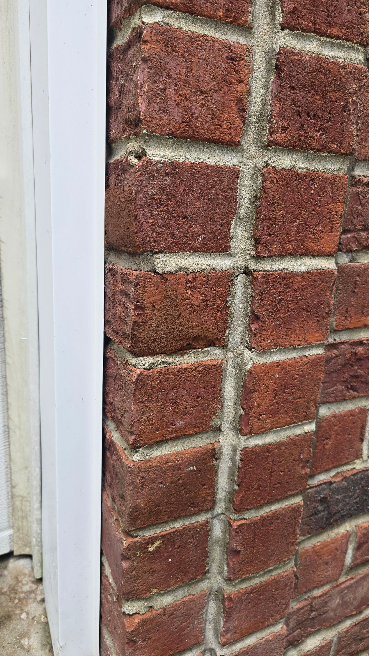 Close-up of a red brick wall with white mortar beside a white painted trim edge