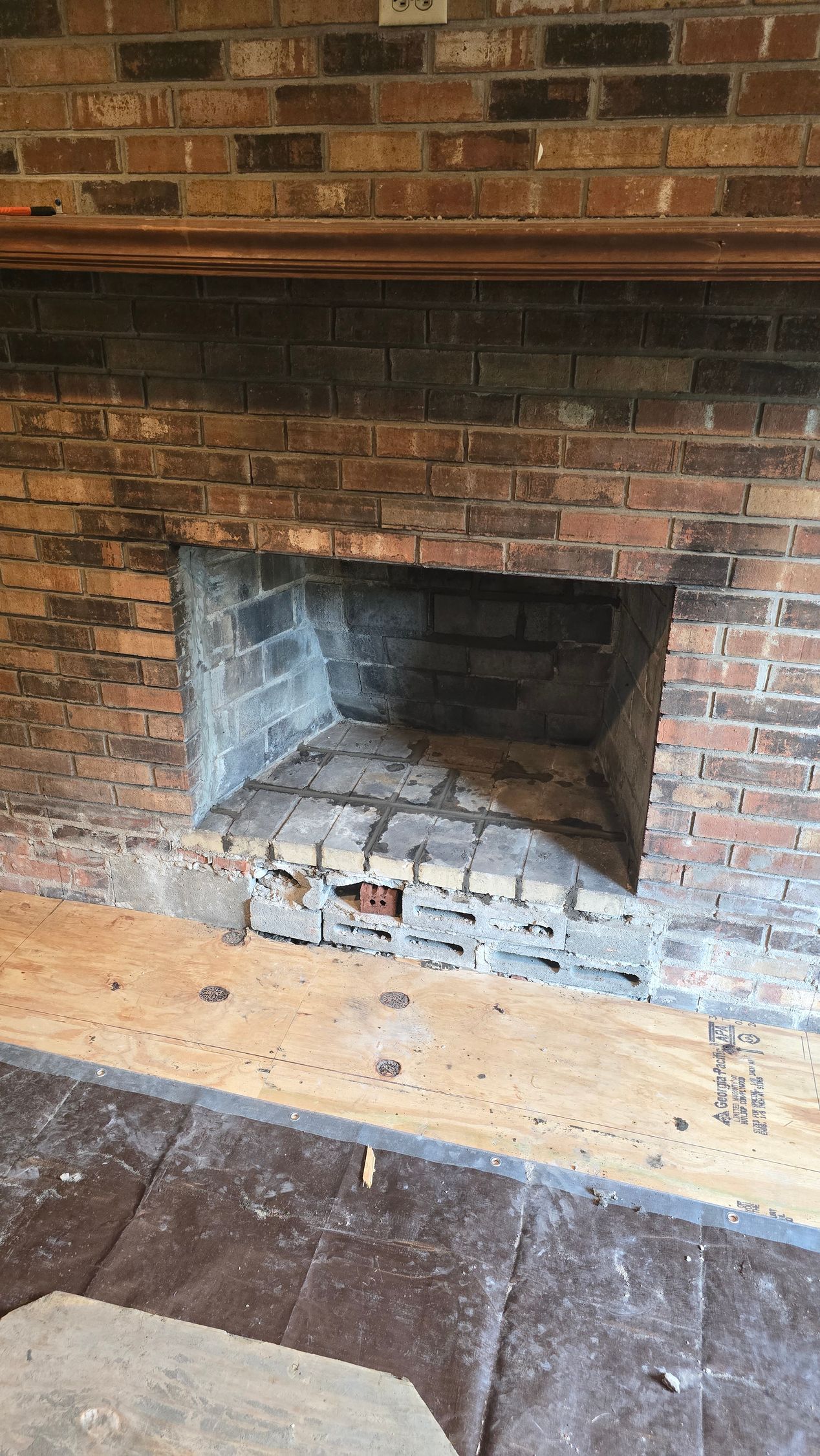 Brick fireplace with a dark, empty firebox and worn hearth in a room.