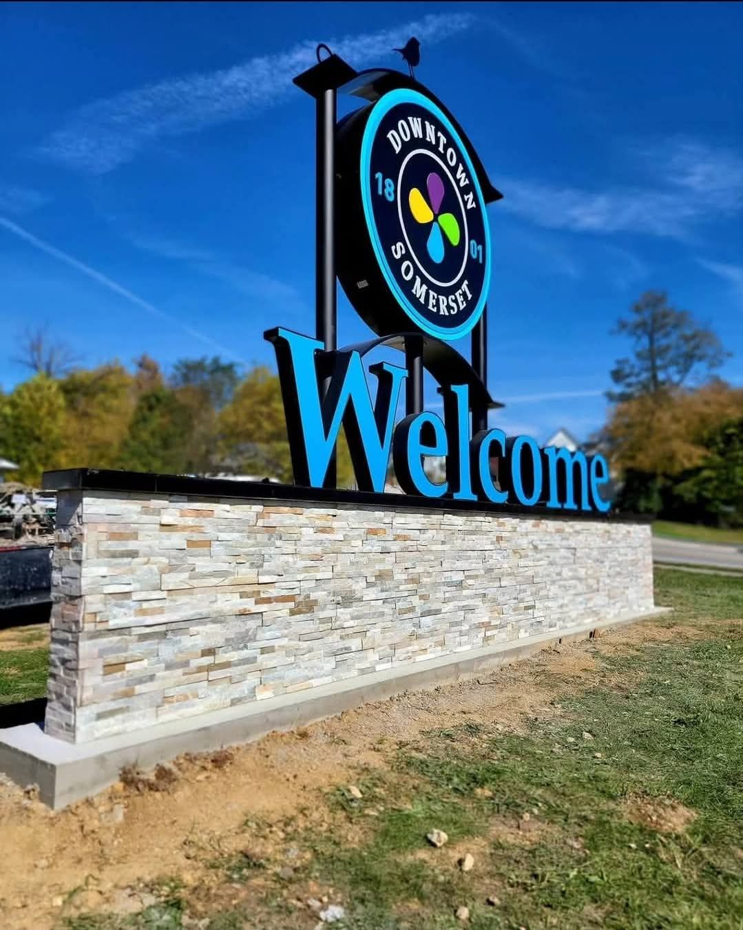 Welcome sign on stone wall with colorful logo under blue sky