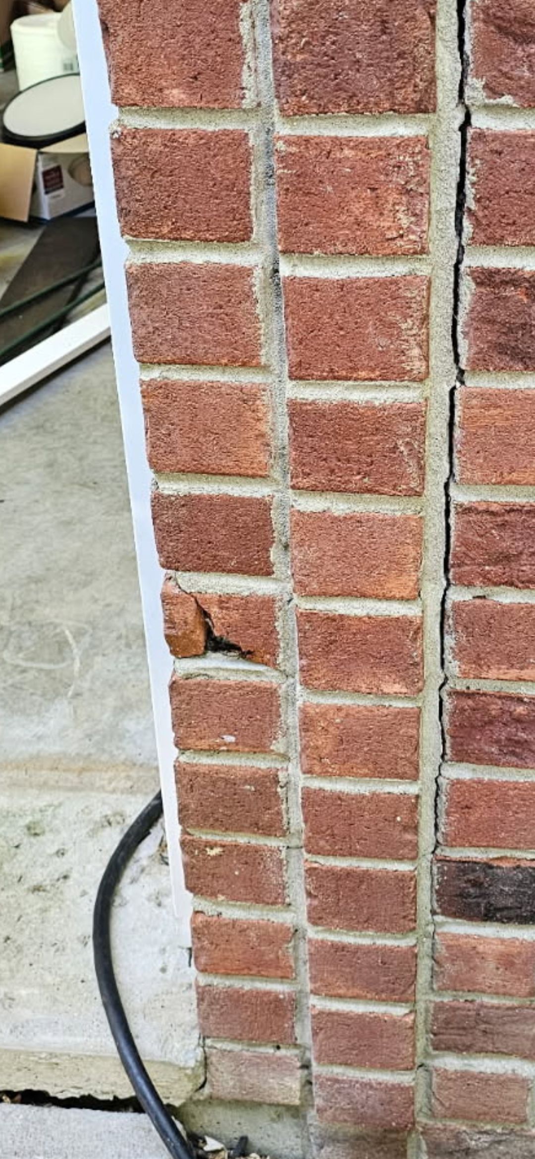 Close-up of a red brick wall corner with white trim and a black cable near the base.