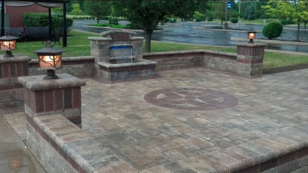 Stone patio with built-in brick benches and lanterns beside a grassy park area